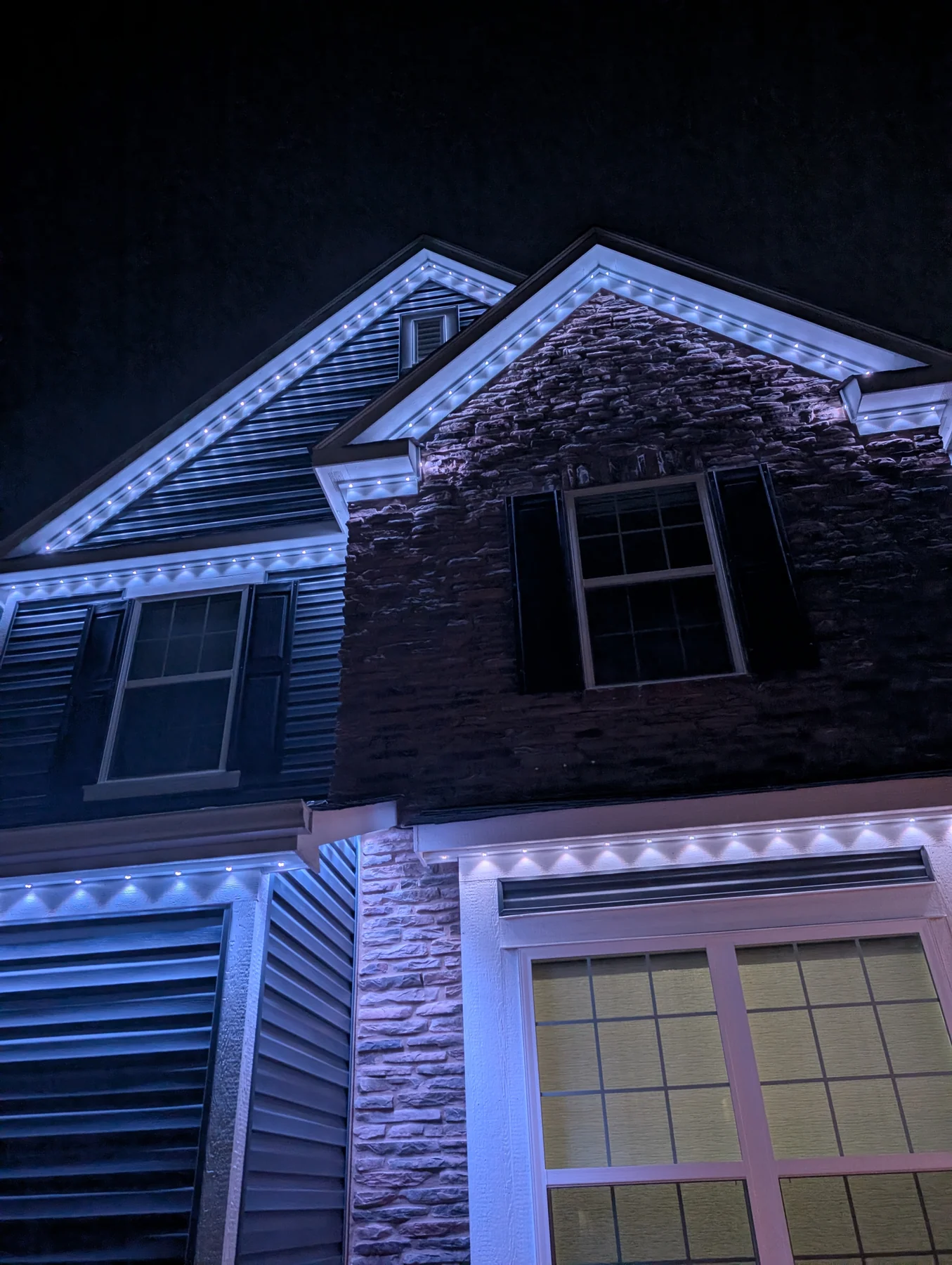 Nighttime photo of a home with back placement, cool white lights hugging tight to the gable peaks tracing the architecture