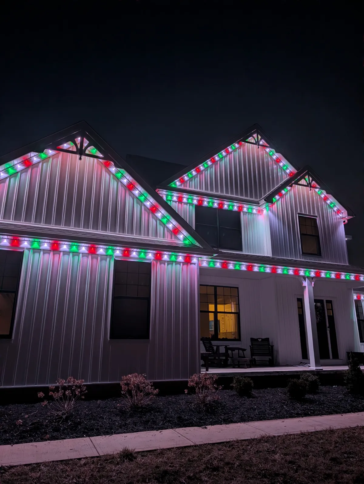 Red and green permanent Christmas lights on modern farmhouse at night