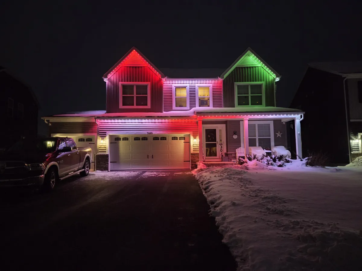 Red and green permanent Christmas lights on two-story home in snow at night