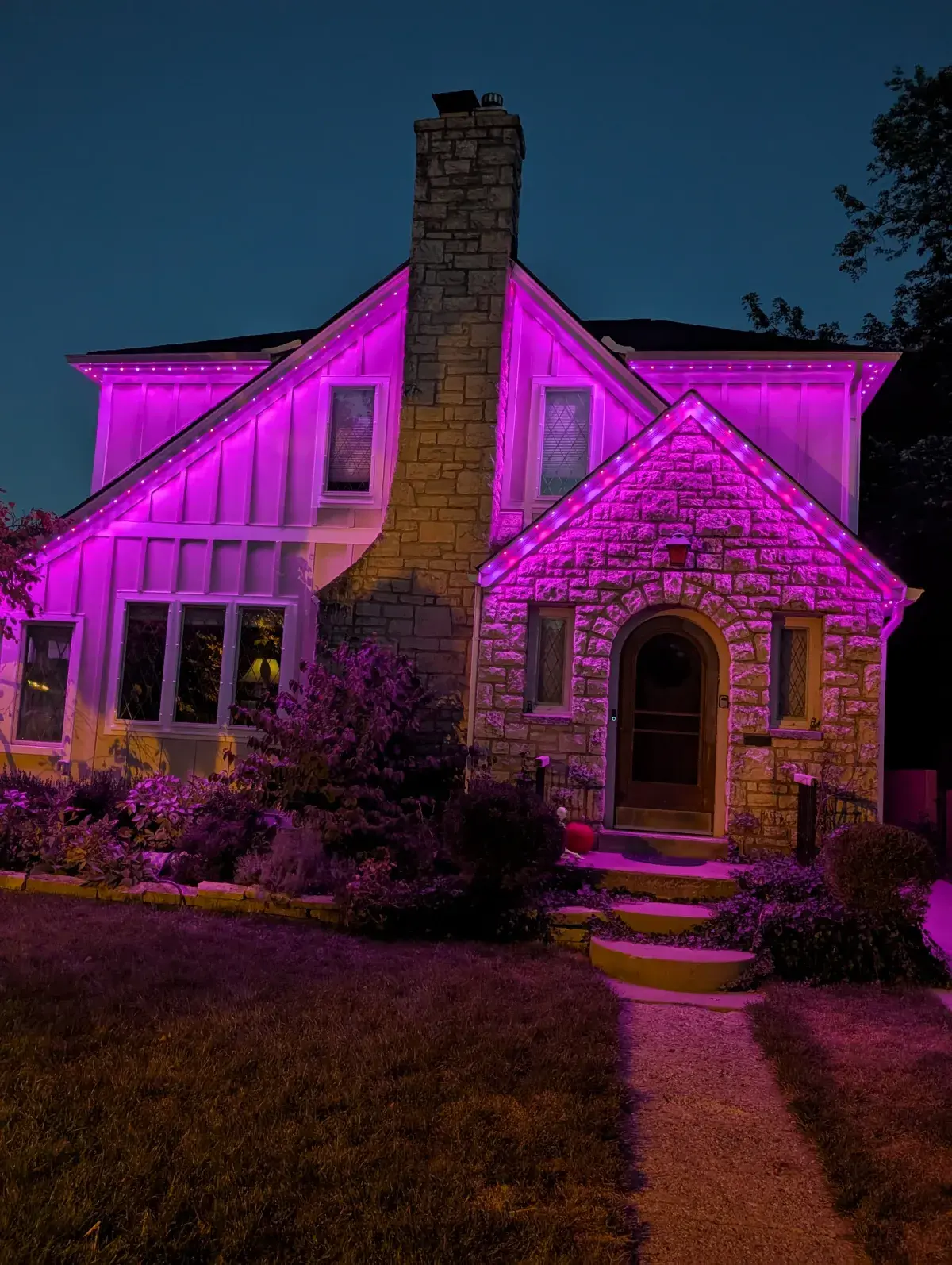 Pink permanent lights on charming stone cottage with chimney at night