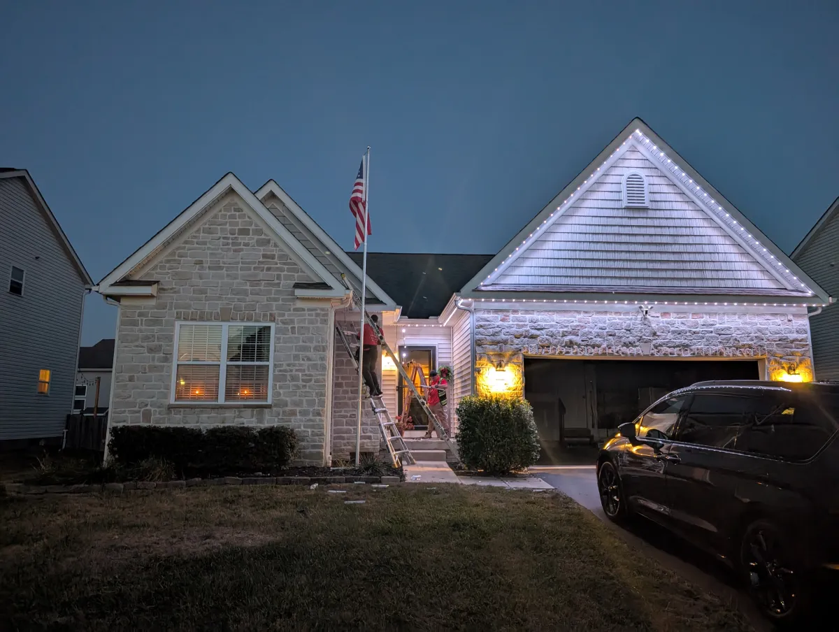White permanent lights on stone ranch home during installation at dusk