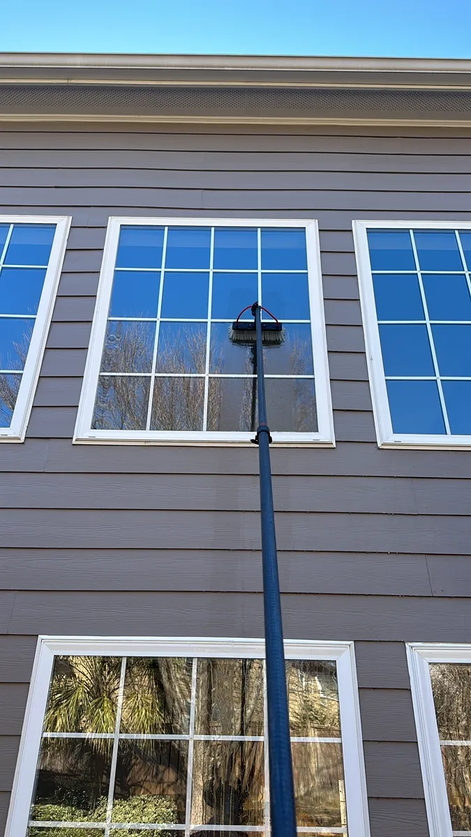 Water fed pole cleaning second floor windows on gray siding home